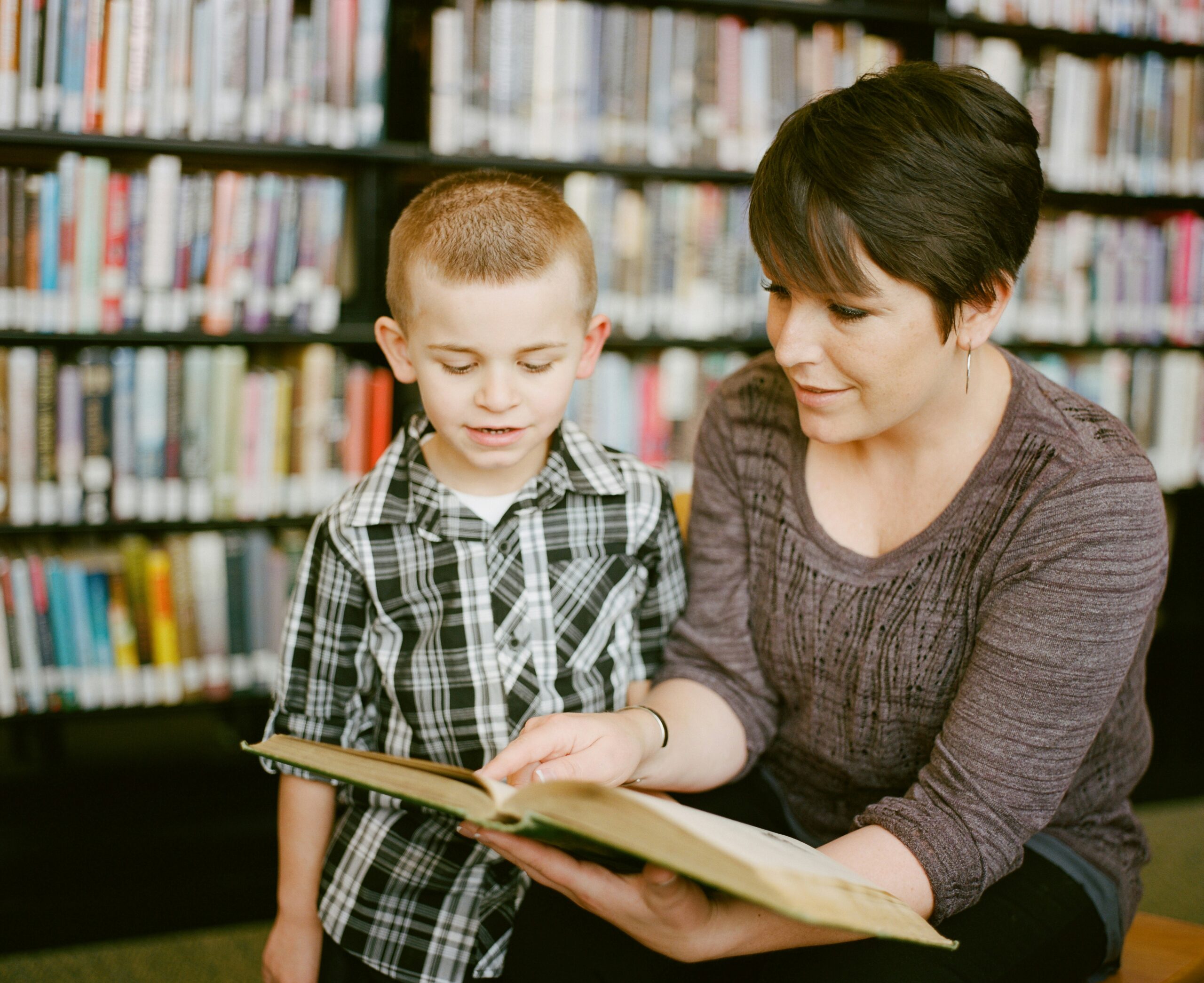 A parent with a child looking at a book in a library